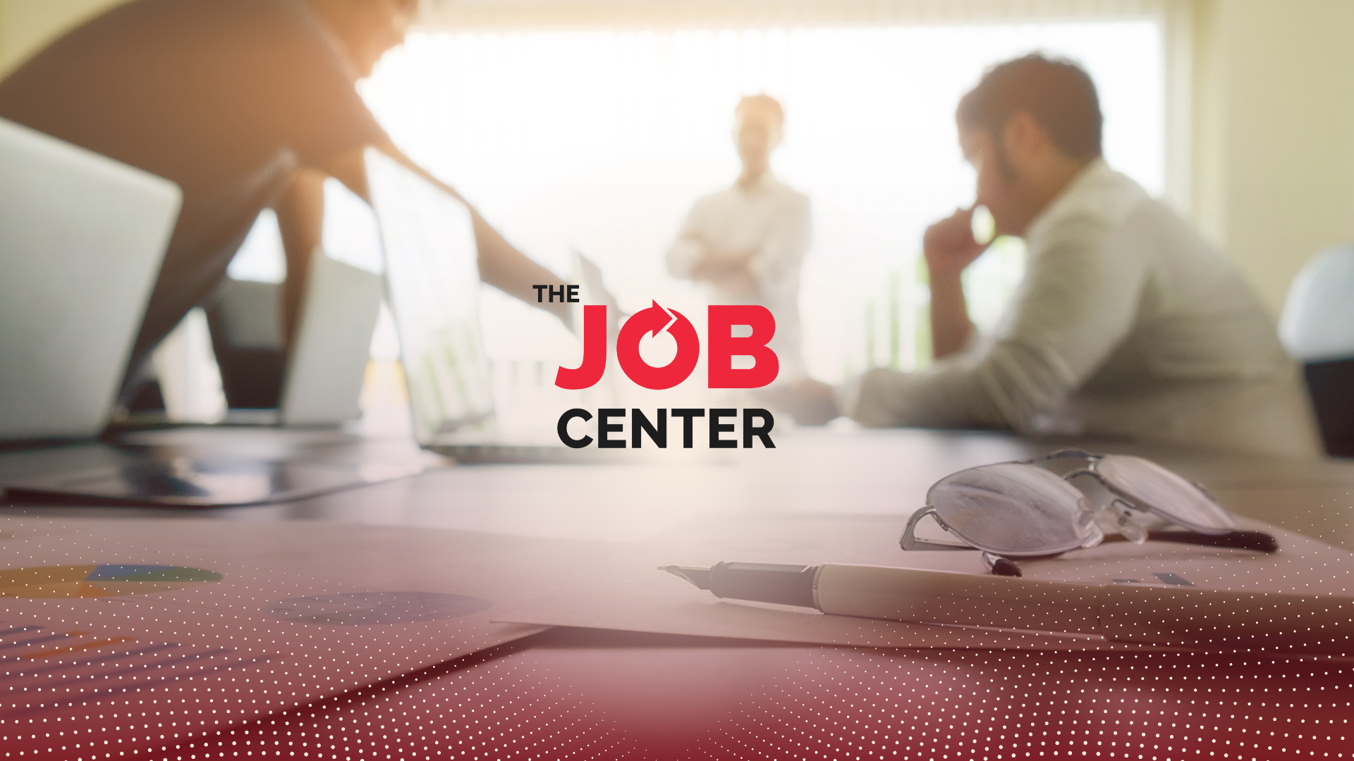 Three men in corporate attire discuss around a conference table with laptops and papers