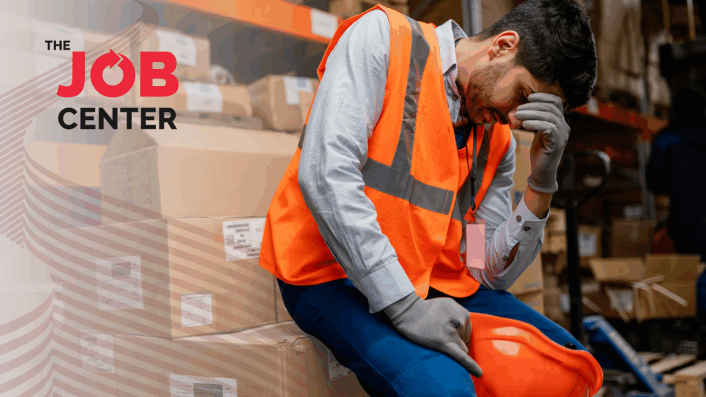 Overwhelmed warehouse worker sits on packaging boxes with head in hand