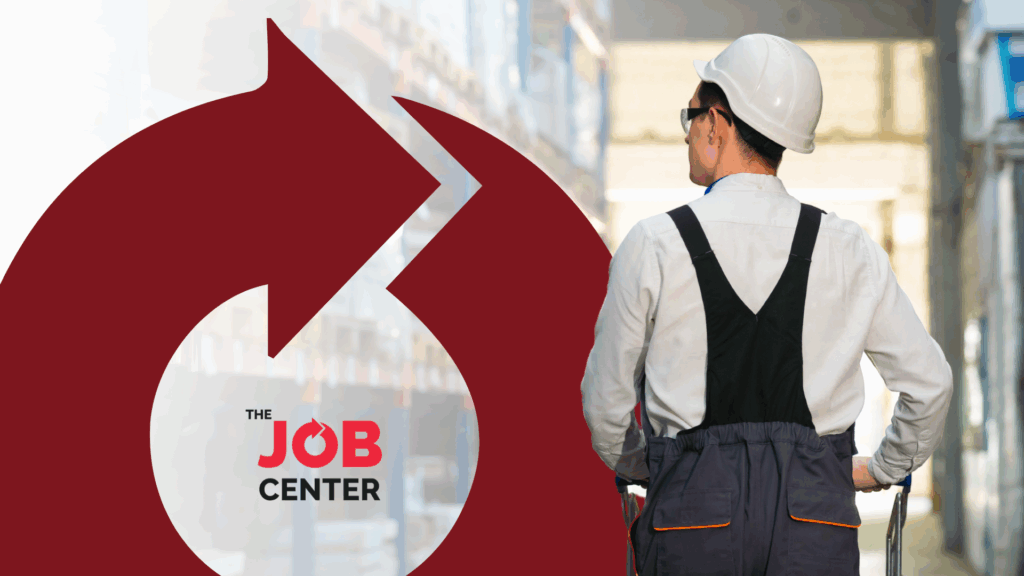 Warehouse worker in hard hat walks through warehouse pushing a trolley